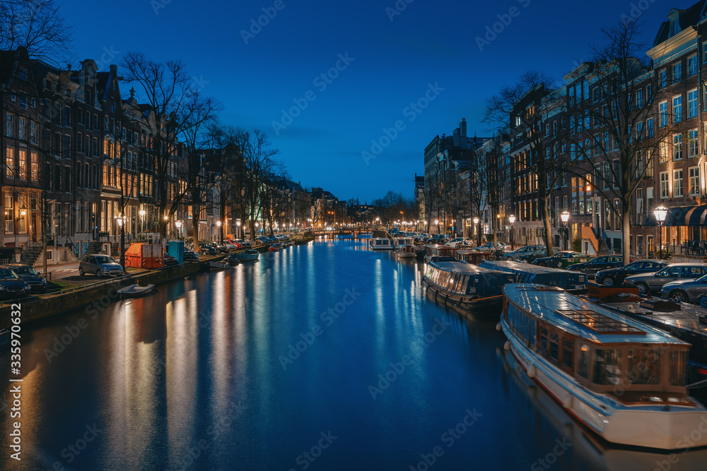 Amsterdam night city skyline at water canal waterfront with boat houses, Amsterdam, Netherlands.