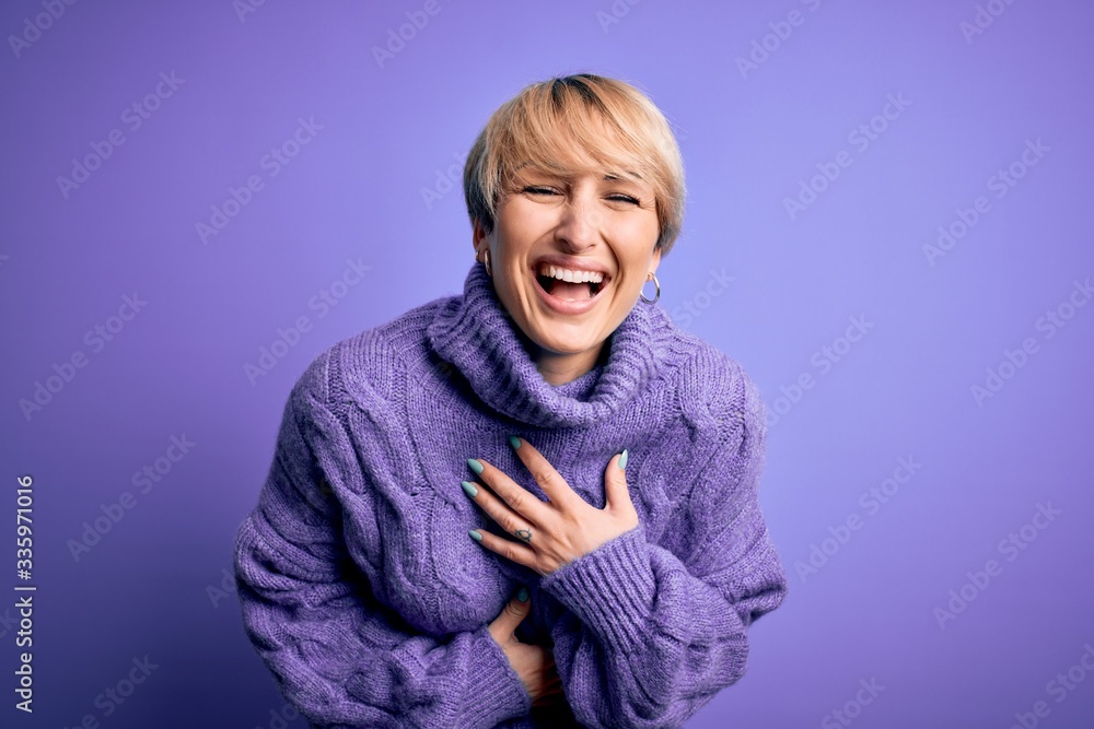 Young blonde woman with short hair wearing winter turtleneck sweater over purple background smiling and laughing hard out loud because funny crazy joke with hands on body. Young blonde woman with short hair wearing winter turtleneck sweater over purple background smiling and laughing hard out loud because funny crazy joke with hands on body.