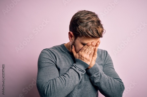 Young handsome blond man with beard and blue eyes wearing casual sweater with sad expression covering face with hands while crying. Depression concept.