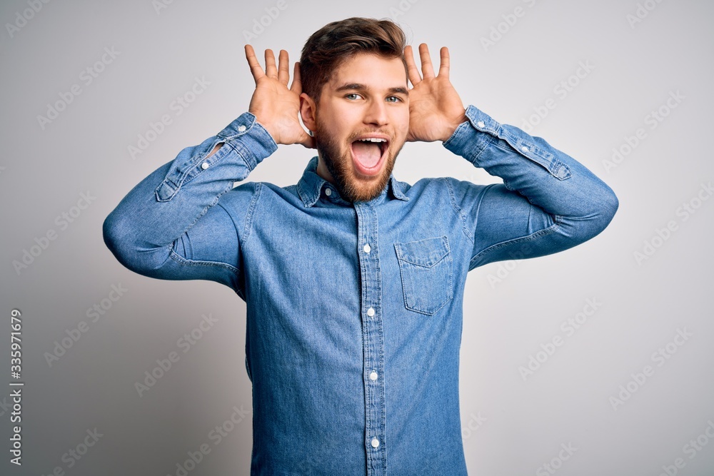 Young handsome blond man with beard and blue eyes wearing casual denim shirt Smiling cheerful playing peek a boo with hands showing face. Surprised and exited Young handsome blond man with beard and blue eyes wearing casual denim shirt Smiling cheerful playing peek a boo with hands showing face. Surprised and exited