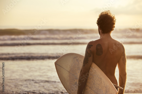 Photography Athletic surfer stands with surfboard at sunset beach