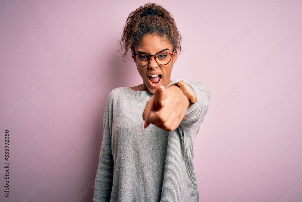 Young beautiful african american girl wearing sweater and glasses over pink background pointing displeased and frustrated to the camera, angry and furious with you Young beautiful african american girl wearing sweater and glasses over pink background pointing displeased and frustrated to the camera, angry and furious with you