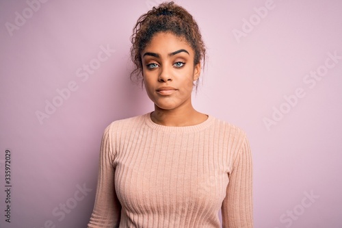 Young beautiful african american girl wearing casual sweater standing over pink background Relaxed with serious expression on face. Simple and natural looking at the camera.
