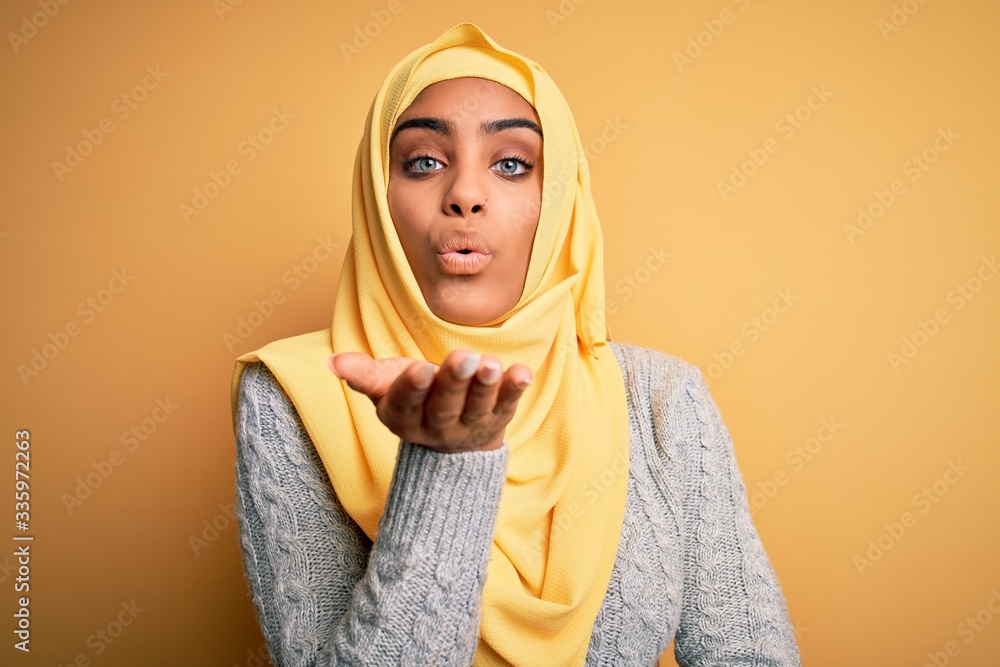 Young beautiful african american girl wearing muslim hijab over isolated  yellow background looking at the camera blowing a kiss with hand on air  being lovely and sexy. Love expression. Stock Photo