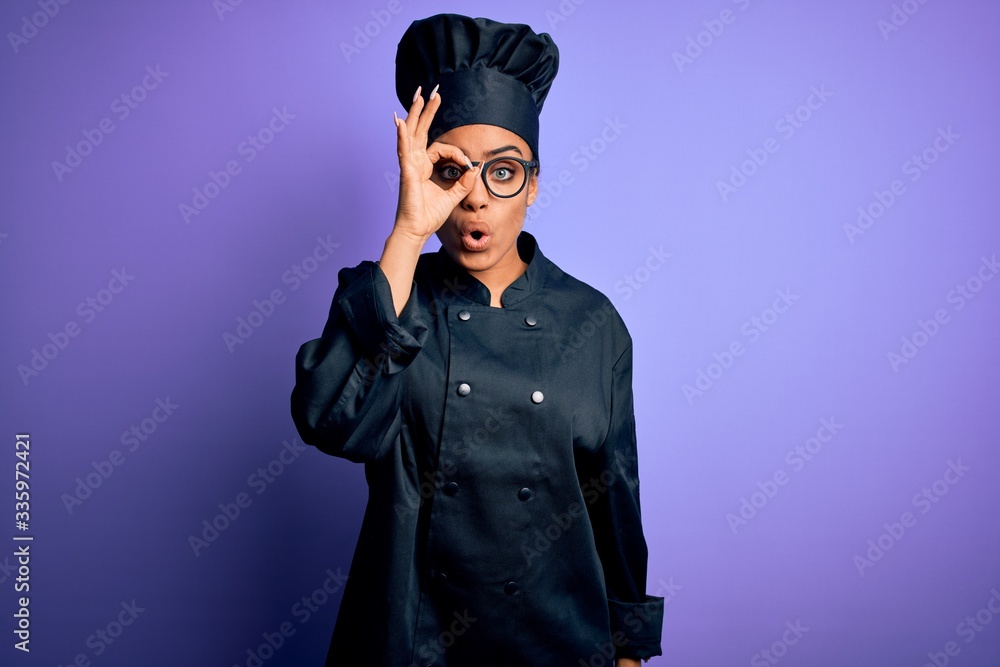Young african american chef girl wearing cooker uniform and hat over purple background doing ok gesture shocked with surprised face, eye looking through fingers. Unbelieving expression. Young african american chef girl wearing cooker uniform and hat over purple background doing ok gesture shocked with surprised face, eye looking through fingers. Unbelieving expression.