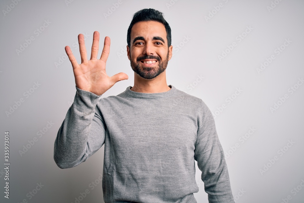 Young handsome man with beard wearing casual sweater standing over white background showing and pointing up with fingers number five while smiling confident and happy. Young handsome man with beard wearing casual sweater standing over white background showing and pointing up with fingers number five while smiling confident and happy.