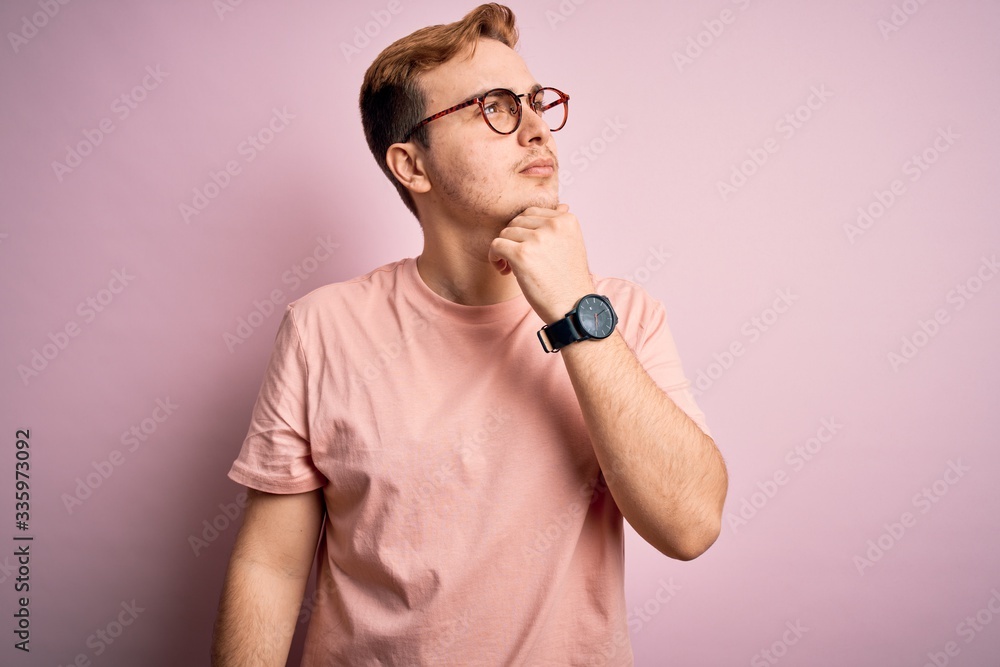 Young handsome redhead man wearing casual t-shirt standing over isolated pink background with hand on chin thinking about question, pensive expression. Smiling with thoughtful face. Doubt concept. Young handsome redhead man wearing casual t-shirt standing over isolated pink background with hand on chin thinking about question, pensive expression. Smiling with thoughtful face. Doubt concept.