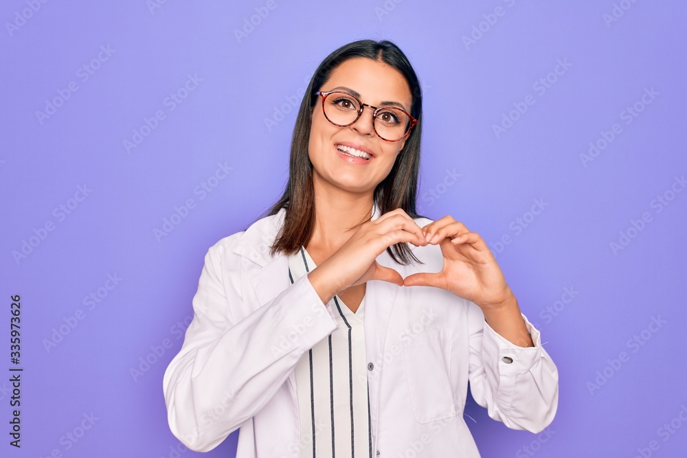 Young beautiful brunette psychologist woman wearing coat and glasses over purple background smiling in love showing heart symbol and shape with hands. Romantic concept. Young beautiful brunette psychologist woman wearing coat and glasses over purple background smiling in love showing heart symbol and shape with hands. Romantic concept.