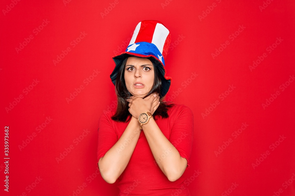 Young beautiful brunette woman wearing united states hat celebrating independence day shouting suffocate because painful strangle. Health problem. Asphyxiate and suicide concept. Young beautiful brunette woman wearing united states hat celebrating independence day shouting suffocate because painful strangle. Health problem. Asphyxiate and suicide concept.