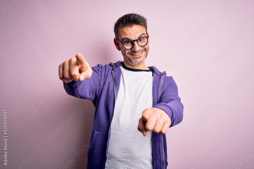 Young handsome man wearing purple sweatshirt and glasses standing over pink background pointing to you and the camera with fingers, smiling positive and cheerful Young handsome man wearing purple sweatshirt and glasses standing over pink background pointing to you and the camera with fingers, smiling positive and cheerful