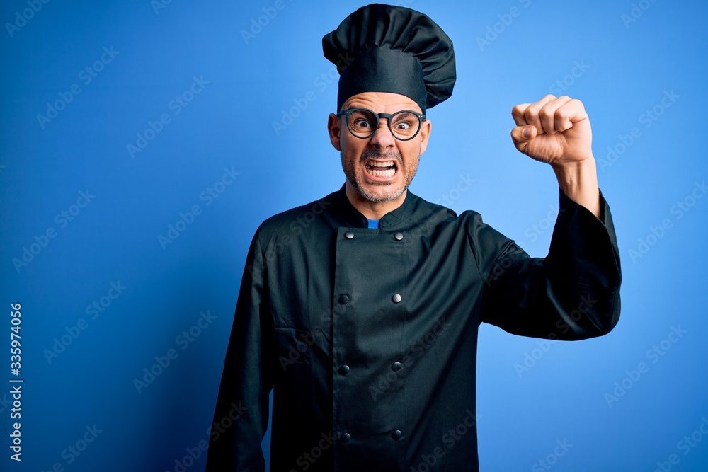 Young handsome chef man wearing cooker uniform and hat over isolated blue background angry and mad raising fist frustrated and furious while shouting with anger. Rage and aggressive concept. Young handsome chef man wearing cooker uniform and hat over isolated blue background angry and mad raising fist frustrated and furious while shouting with anger. Rage and aggressive concept.