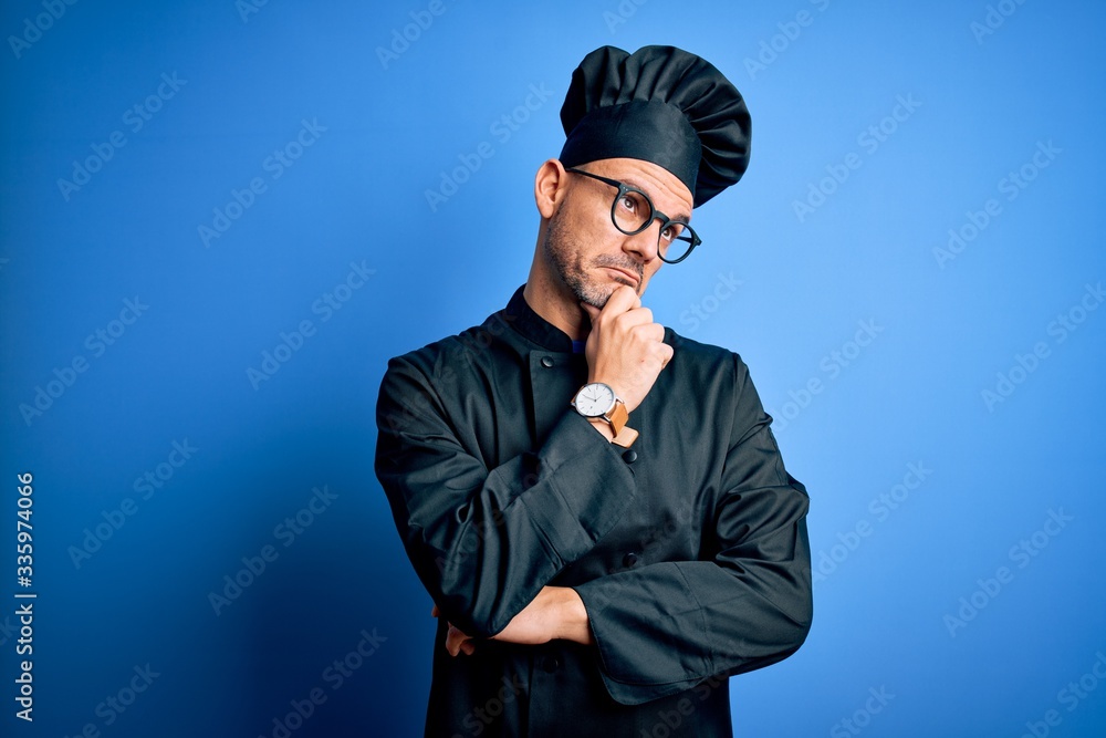 Young handsome chef man wearing cooker uniform and hat over isolated blue background Thinking worried about a question, concerned and nervous with hand on chin Young handsome chef man wearing cooker uniform and hat over isolated blue background Thinking worried about a question, concerned and nervous with hand on chin