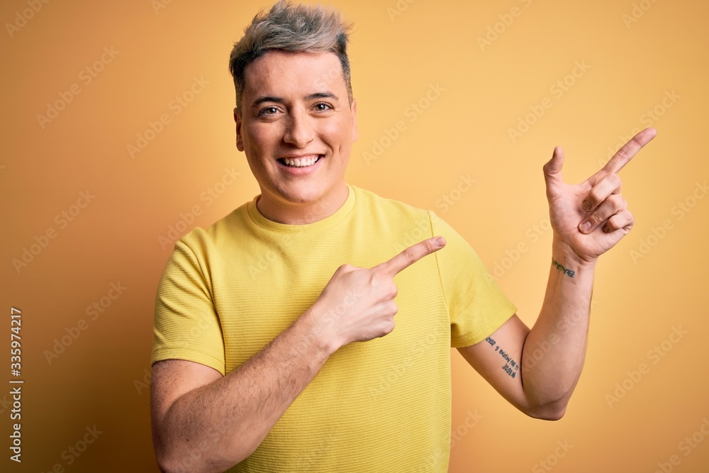 Young handsome modern man wearing yellow shirt over yellow isolated background smiling and looking at the camera pointing with two hands and fingers to the side.
