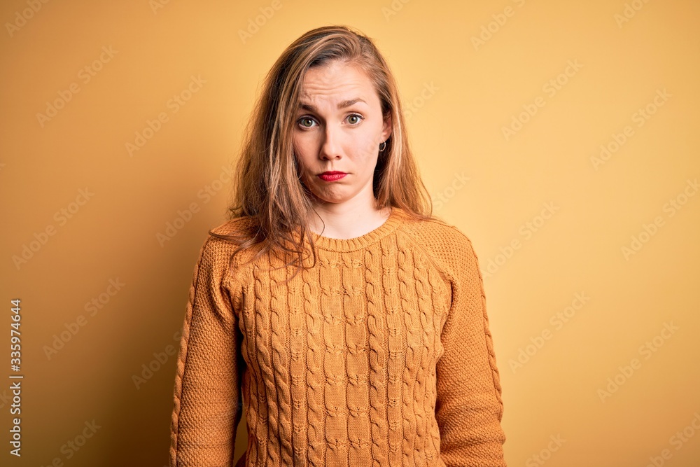 Young beautiful blonde woman wearing casual sweater standing over yellow background skeptic and nervous, frowning upset because of problem. Negative person. Young beautiful blonde woman wearing casual sweater standing over yellow background skeptic and nervous, frowning upset because of problem. Negative person.