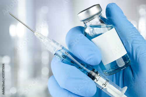 Healthcare concept with a hand in blue medical gloves holding a vaccine vial with blue liquid and black white label