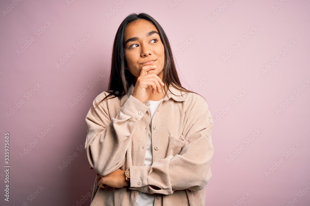 Young beautiful asian woman wearing casual shirt standing over pink background with hand on chin thinking about question, pensive expression. Smiling with thoughtful face. Doubt concept. Young beautiful asian woman wearing casual shirt standing over pink background with hand on chin thinking about question, pensive expression. Smiling with thoughtful face. Doubt concept.