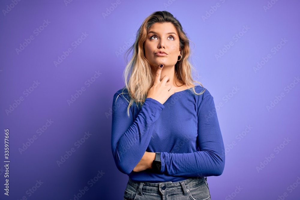 Young beautiful blonde woman wearing casual t-shirt over isolated purple background Thinking concentrated about doubt with finger on chin and looking up wondering Young beautiful blonde woman wearing casual t-shirt over isolated purple background Thinking concentrated about doubt with finger on chin and looking up wondering