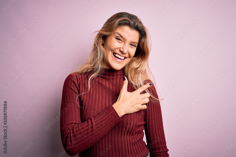 Fototapeta premium Young beautiful blonde woman wearing casual sweater over isolated pink background cheerful with a smile of face pointing with hand and finger up to the side with happy and natural expression on face