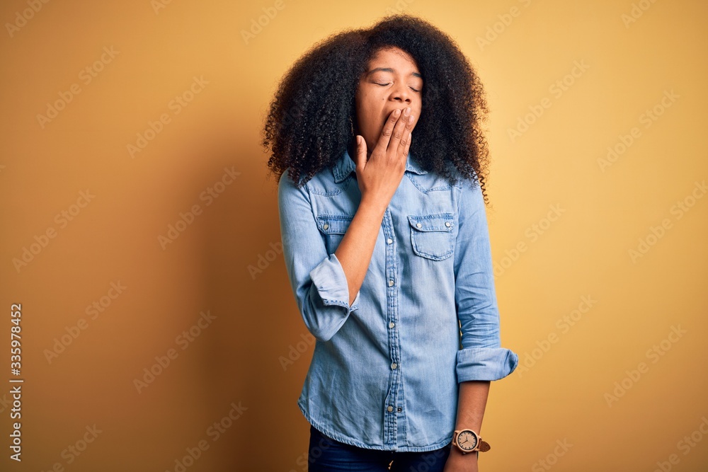 Young beautiful african american woman with afro hair standing over yellow isolated background bored yawning tired covering mouth with hand. Restless and sleepiness. Young beautiful african american woman with afro hair standing over yellow isolated background bored yawning tired covering mouth with hand. Restless and sleepiness.
