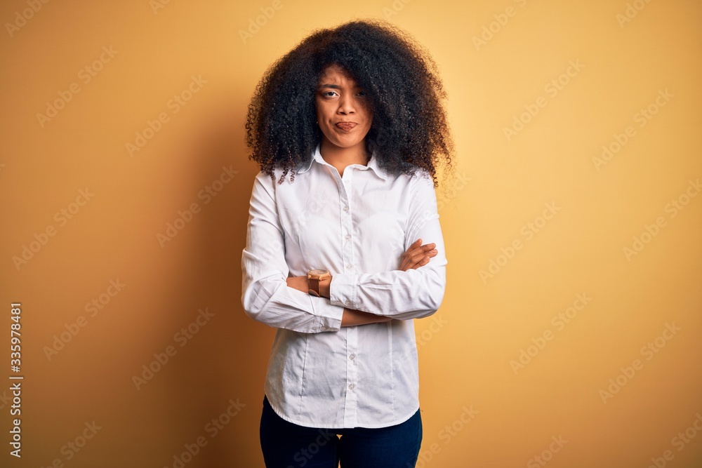 Young beautiful african american elegant woman with afro hair standing over yellow background skeptic and nervous, disapproving expression on face with crossed arms. Negative person. Young beautiful african american elegant woman with afro hair standing over yellow background skeptic and nervous, disapproving expression on face with crossed arms. Negative person.