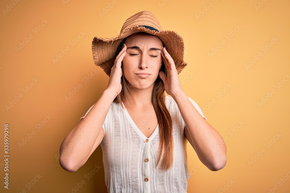 Young beautiful woman wearing casual t-shirt and summer hat over isolated yellow background suffering from headache desperate and stressed because pain and migraine. Hands on head. Young beautiful woman wearing casual t-shirt and summer hat over isolated yellow background suffering from headache desperate and stressed because pain and migraine. Hands on head.