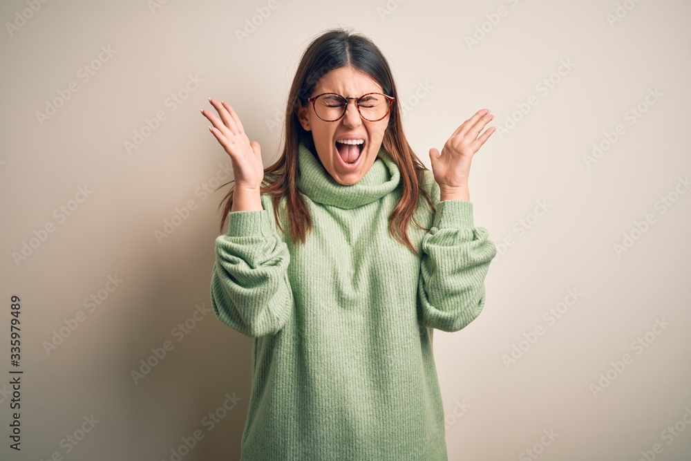 Young beautiful woman wearing casual sweater standing over isolated white background celebrating mad and crazy for success with arms raised and closed eyes screaming excited. Winner concept Young beautiful woman wearing casual sweater standing over isolated white background celebrating mad and crazy for success with arms raised and closed eyes screaming excited. Winner concept