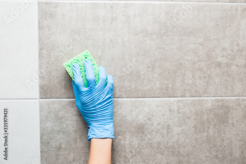 cleaning the toilet room, a hand in a blue glove washes a tile.