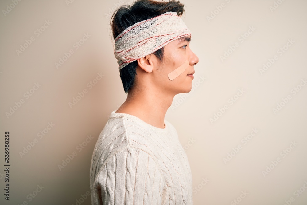 Young handsome chinese man injured for accident wearing bandage and strips on head looking to side, relax profile pose with natural face and confident smile. Young handsome chinese man injured for accident wearing bandage and strips on head looking to side, relax profile pose with natural face and confident smile.