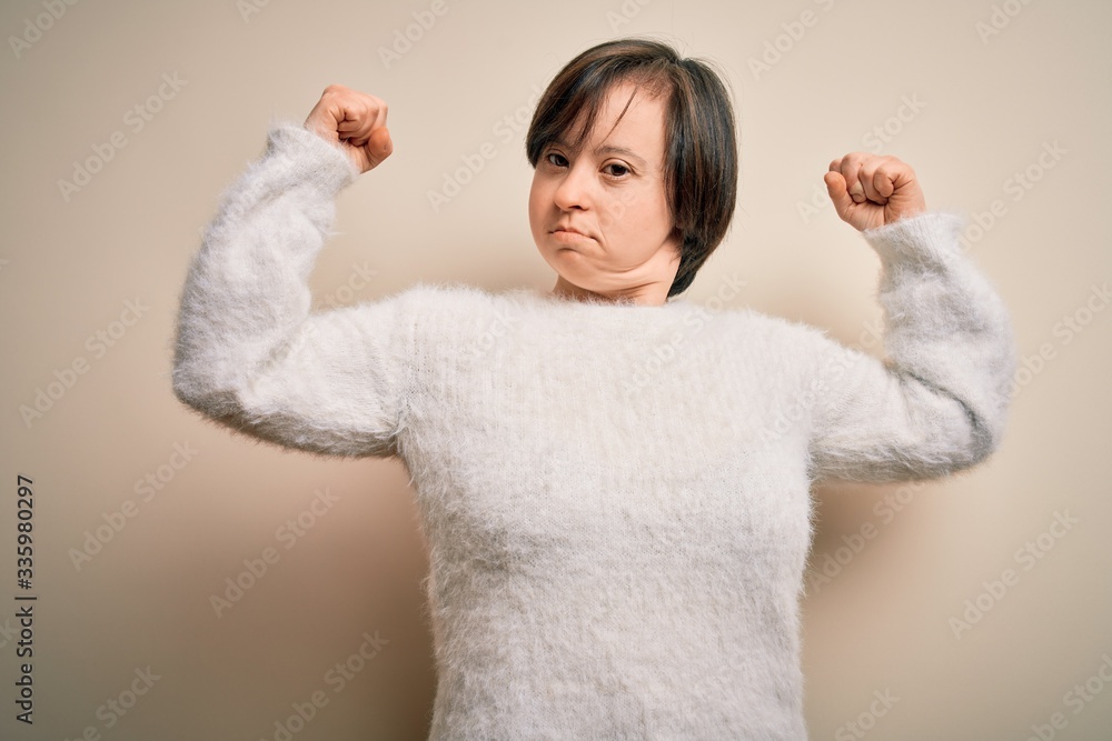 Young down syndrome woman standing over isolated background showing arms muscles smiling proud. Fitness concept. Young down syndrome woman standing over isolated background showing arms muscles smiling proud. Fitness concept.