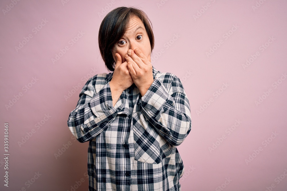 Young down syndrome woman wearing casual shirt over pink background shocked covering mouth with hands for mistake. Secret concept. Young down syndrome woman wearing casual shirt over pink background shocked covering mouth with hands for mistake. Secret concept.