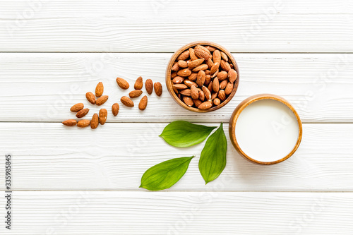 Almond milk near nuts on white wooden background top-down