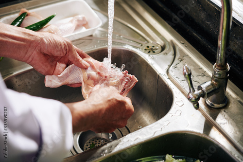 Foto Hands of man rinsing chicken thigh under tap water