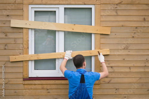Fotografie a worker in a blue uniform, boarded up the window of a wooden house, from thieve