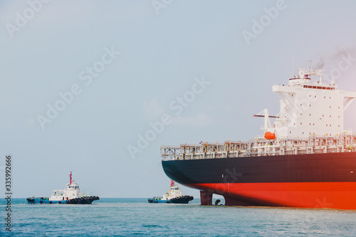 Stern Cargo container ship in the sea during go on dock by two tugboat assistance drug stern ship and connecting in shipyard.