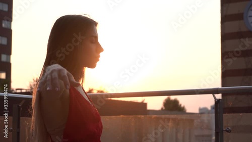 Beautiful young girl dancing on the street of a modern city in the sunset light. She is wearing a red dress. Slow motion.