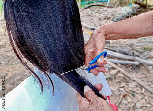 Women cutting hair by her mother, mom cut the hair of her daughter, hairdressing under the shade of a large tree, homemade hair cut ends, with scissors and a comb, close up photography.