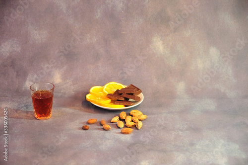 Crystal glass of cognac, a plate with lemon slices and chocolate on a gray background, rad a scattering of almonds. photo