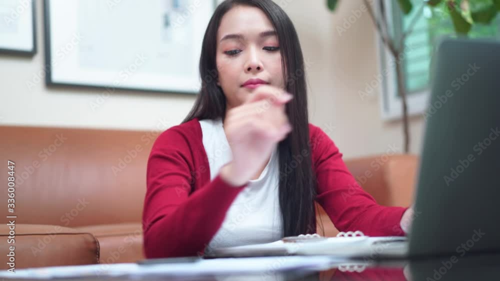 Young beautiful Asian woman using computer laptop and receive cell phone while relaxing in the living room (Camera handheld and movement technique) Young beautiful Asian woman using computer laptop and receive cell phone while relaxing in the living room (Camera handheld and movement technique)