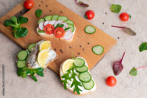 A set of sandwiches with sprats, homemade curd cream with herbs, with radishes, cucumbers, and tomatoes, on a wooden background. Top view. Copy space.