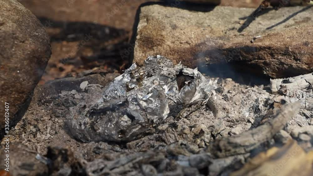 Man picking up baked potatoes with a knife from a aluminium foil laying in a fireplace. Man picking up baked potatoes with a knife from a aluminium foil laying in a fireplace.