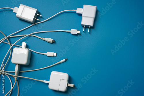 Top view or flat lay of White mobile power charger and USB in multiple types laid disorderly and mess on blue pvc sheet texture background , energy management concept ,with copy space
