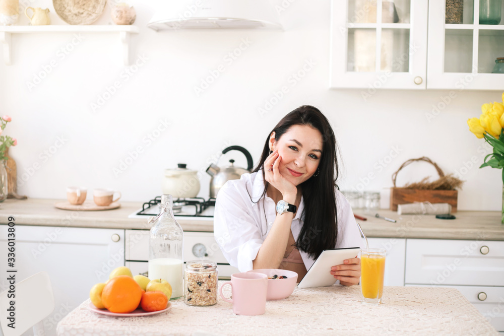 Young beautiful woman using digital tablet while breakfast in kitchen.