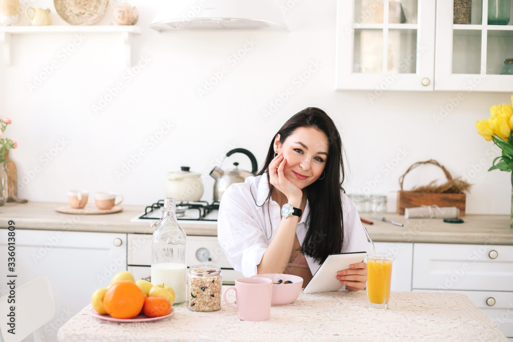 Young beautiful woman using digital tablet while breakfast in kitchen. Young beautiful woman using digital tablet while breakfast in kitchen.