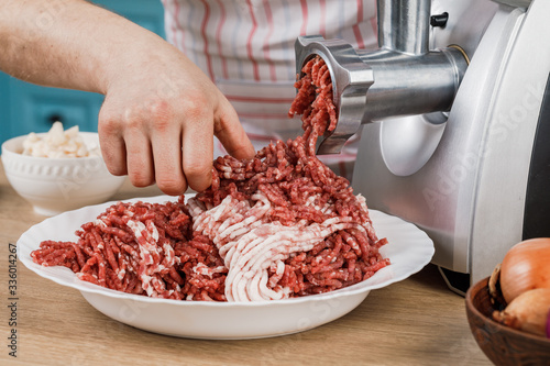 Raw meat. The process of preparing minced meat is carried out using a meat grinder. A male chef uses a meat grinder in the kitchen.