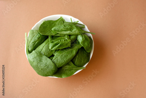 Plate of raw fresh spinach leaves on beige background
