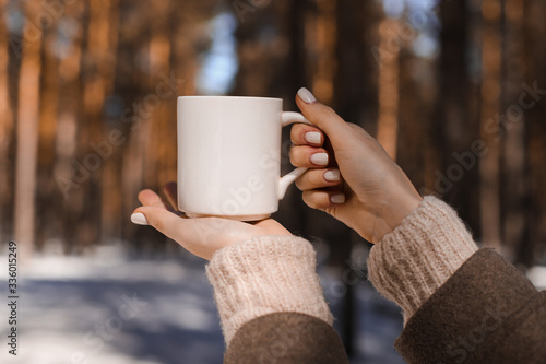 Female hands hold a white mug against the background of the spring forest.