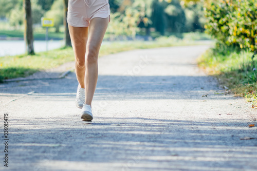 Young woman legs in shorts running in the park. Running training in spring, summer. Outdoor fitness.