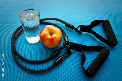 Sport expander, glass with water and an apple on blue yoga mat background photo