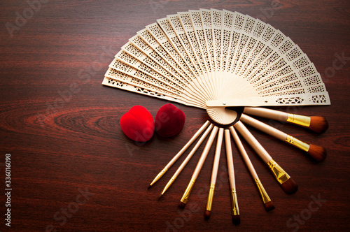 Many makeup brushes and two red hearts on the wooden table