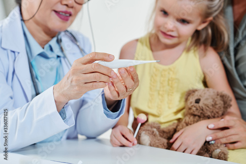Pediatrician showing electronic thermometer to little girl and explaining what temperature she has